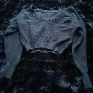 Svart ribbad tröja från Gina Tricot - Säljer en snygg svart ribbad tröja från Gina Tricot i storlek XS. Tröjan har en v-ringad design och är croppad med långa ärmar. Perfekt för en stilren look.