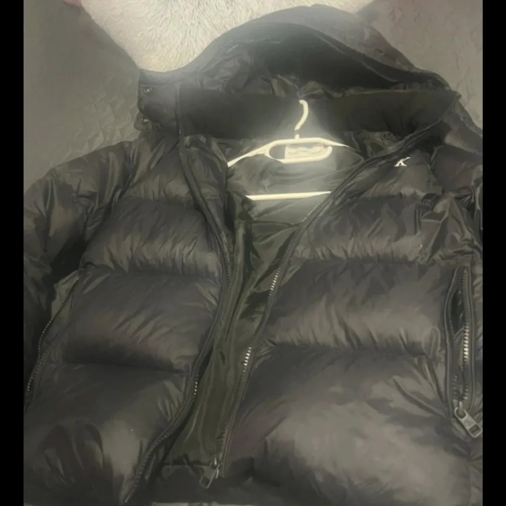 Säljer en snygg svart dunjacka från Calvin Klein Jeans. Jackan har en dragkedja framtill och är perfekt för kyliga dagar. Den har en klassisk design med CK-logga på bröstet och ärmarna. Perfekt för dig som vill ha stil och komfort i ett. Jackan är I väldigt fin skick köpte föra året från Nelly. Liten highlighter på armen i bilden 3. . Takit.