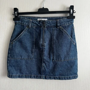 Jeanskjol från M&S - Säljer en snygg jeanskjol från M&S i klassisk blå denim. Kjolen har en dragkedja framtill och praktiska fickor. Perfekt för en avslappnad stil.