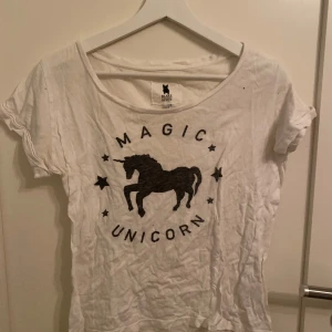 Vit t-shirt med enhörningstryck från Blake Seven - Säljer en vit t-shirt från Blake Seven med ett coolt tryck av en enhörning och texten 'Magic Unicorn'. T-shirten har korta ärmar och en rund halsringning. Perfekt för en avslappnad stil tillsammans med ett par sköna svarta shorts!