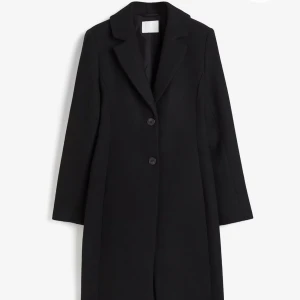Svart kappa med knappar - Elegant svart kappa med två knappar framtill. Klassisk design med långa ärmar och en stilren krage. Perfekt för en sofistikerad look. Helt slutsåld och i fint skick, endas använd några gånger i veckan i 2 månader ca. Nypris 900kr