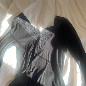 Svart långärmad topp med spetsdetaljer - Snygg svart långärmad topp med spetsdetaljer vid halsringningen. Perfekt för en stilren look. Toppen har en åtsittande passform och är tillverkad i ett mjukt material. Köpt från pieces men är identiskt med intimissmi tröjan 