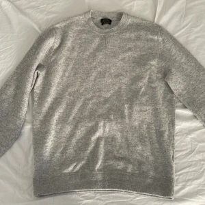 Grå tröja från Massimo Dutti - Säljer en stilren grå tröja från Massimo Dutti, tillverkad i merinoull och extra fin bomull. Tröjan har en klassisk rund halsringning och ribbade muddar vid ärmslut och nederkant. Perfekt för en elegant och bekväm look. Tröjan är använd två gånger då den är för kort i midjan på mig. Den är storlek L men sitter mer som M. Passar perfekt för dig som är mellan 170-187 lång 