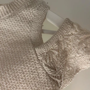 Beige stickad topp från Lindex - Säljer en söt beige stickad topp från Lindex. Den har korta ärmar och fina spetsdetaljer vid ärmslut och nederkant. Perfekt för en stilren look!