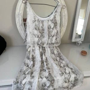 Bar III vit klänning, storlek S - Snygg ärmlös klänning från Bar III i vitt och grått med ett unikt mönster. Tillverkad i 100% polyester, perfekt för en stilren look. Klänningen har en luftig passform och är knälång, vilket gör den bekväm och lätt att bära.storlek på längd 90cm