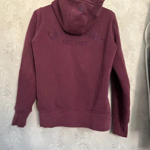 Vintage Sail racing zip hoodie - Säljer nu denna snygga vintage zip hoodien ifrån Sail racing, köpte för något år sedan här på Plick av en annan säljare. Den är i en snygg vin röd färg med både tryck på ryggen men även på bröstet. Den har även silver dragkedja mm, det går att båda lägre och jag är öppen för förslag❤️ skriv för mer frågor eller bilder🥰