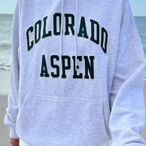 Grå hoodie från Brandy Melville - Säljer en grå hoodie från Brandy Melville med texten 'Colorado Aspen' i mörkgrönt framtill. Den har en klassisk känguruficka och justerbar huva med dragsko. Perfekt för en avslappnad stil!