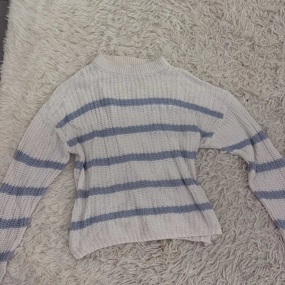 Säljer en mysig vit stickad tröja med blå ränder. Tröjan har en avslappnad passform och långa ärmar, perfekt för kyligare dagar. Den är både stilren och bekväm, idealisk för en casual look.. Neuletakit & Villapaidat.
