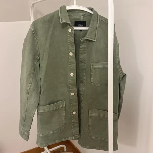 Grön overshirt från Rails - Säljer en stilren grön overshirt från Rails i storlek M. Jackan har knappar framtill och stora fickor, perfekt för en avslappnad look. Den är långärmad och gjord i ett bekvämt material.