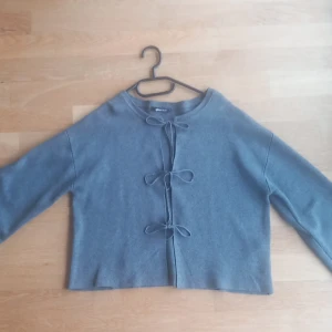 Grå kofta från Gina Tricot - Säljer en stilren grå kofta från Gina Tricot i storlek S. Koftan har knytband framtill och är tillverkad i ett mjukt material. Perfekt för en avslappnad look.