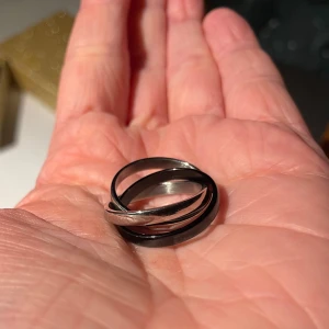 *NY*Trippelring i silver och svart stl 17/18 - Elegant ring med tre sammanflätade ringar i silver och svart. En stilren accessoar som passar till alla tillfällen.  Enligt säljaren i rostfritt stål.  Ny, bara provad, för stor för mig som har stl 16,5, uppskattar att på pekfingret passar stl 17-17,5 bäst och på ringfingret 17,5-18.