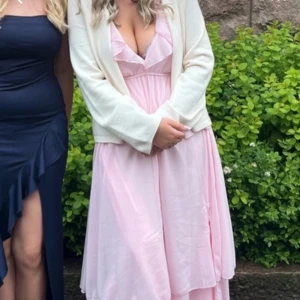 Ljusrosa långklänning med volangdetaljer - Elegant ljusrosa långklänning med v-ringad design och volangdetaljer. Perfekt för sommarens festligheter. Klänningen har en luftig passform och är tillverkad i ett lätt material som ger en romantisk känsla. Perfekt till balen💗kan sänka priset!