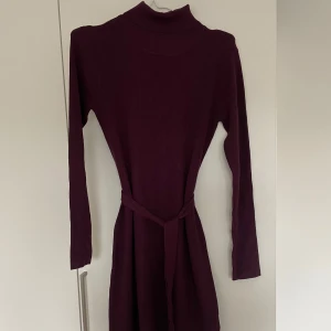 Mörklila/mörk öd klänning från Bodyflirt - Snygg mörklila klänning från Bodyflirt i ribbat material. Klänningen har långa ärmar och en knytning i midjan för en smickrande passform. Perfekt för kyligare dagar med sin mysiga och stilrena design.  Storlek S. 36/38 passar även M 