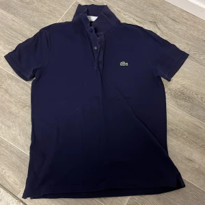 Mörkblå pikétröja från Lacoste - Säljer en stilren mörkblå pikétröja från Lacoste använd 3-4 gånger säljer pgd av den e lite för stor den är size M och jag som säljer den är 161cm lång så skulle hade sagt att den är perfekt för personer mellan 165-175 ny pris är 1200kr 