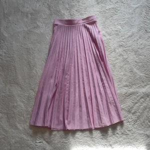 Rosa plisserad kjol - Säljer en söt rosa plisserad kjol som är perfekt för vår och sommar. Kjolen har en elegant midilängd och ett bekvämt elastiskt midjeband. Den är gjord i ett lätt och luftigt material som ger en fin rörelse när du går. Passar utmärkt till både vardag och speciella tillfällen.