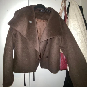 Brun kappa från Gina Tricot - Snygg brun kappa från Gina Tricot med stora slag och knappar framtill. Perfekt för höst och vår. Jackan har en elegant design med en lös passform och långa ärmar.