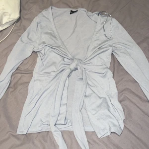 Ljusblå omlottopp från Gina Tricot - Säljer en superfin ljusblå omlottopp från Gina Tricot i storlek XXS. Toppen har långa ärmar och en snygg knytning framtill som ger en elegant look. Perfekt för både vardag och fest! 💙säljer för 200