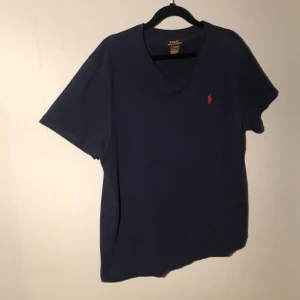 Ralph lauren v-ringad T-shirt mörk blå. -  Ralph Lauren mörkblå t-shirt i mjuk bomull med V-ringad. Klassisk passform och stilren design. Perfekt för både vardag och avslappnade tillfällen – ett tidlöst basplagg.Den har också inga hål eller fläckar. Jag kan diskutera priset.