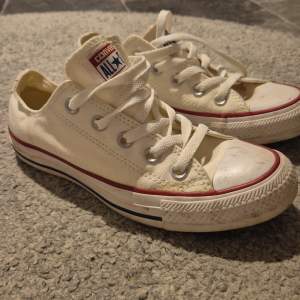 Säljer ett par klassiska vita Converse All Star sneakers i bra skick. De har den ikoniska röda och blå randen runt sulan och snörning framtill. Perfekta för en avslappnad stil och passar till det mesta i garderoben.