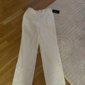 Vita kostymbyxor från NA-KD - Säljer ett par stilrena vita kostymbyxor från NA-KD i storlek S. Byxorna har en klassisk design med hög midja och raka ben, perfekt för både vardag och fest. De är helt nya med tag kvar!