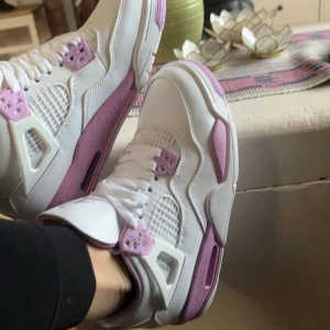 Nike Air Jordans i vitt och rosa - Säljer ett par snygga Nike Jordans pink oreo.   Skorna har en cool design med rosa detaljer och vit bas. Perfekta för att sticka ut i mängden! De är i mycket bra skick/har aldrig använt dom och har klassisk snörning.
