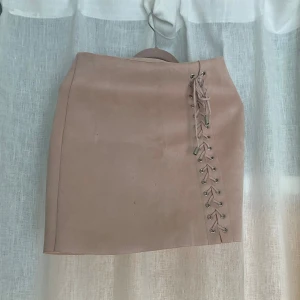 Beige kjol från Bik Bok - Säljer en superfin rosa beige kjol från Bik Bok i storlek XS. Kjolen har en snygg snörning på sidan som ger den en unik touch. Perfekt för både vardag och fest! 🥰