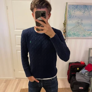 Mörkblå stickad tröja från Polo Ralph Lauren - Säljer en snygg mörkblå stickad tröja från Polo Ralph Lauren. Den har ett klassiskt kabelstickat mönster och en liten grön logga på bröstet. Perfekt för höst och vinter, med långa ärmar och ribbade muddar. Passar både till vardags och lite finare tillfällen. 🧶💙Är L i ungdomstorlek men passar xs och kanske s i vuxenstorlek!