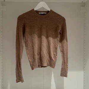 Beige/brun tröja från Zara - Säljer en snygg beige tröja från Zara i mycket bra skick. Den är långärmad och har stilrena knappar vid ärmsluten. Perfekt för höst och vår, och passar både till vardags och lite finare tillfällen. Supermjuk och bekväm att ha på sig!