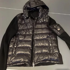 Moncler cardigan  - Säljer en snygg svart pufferjacka från Moncler. Den har en quiltad design med dragkedja och en praktisk huva. Ärmarna är långärmade och gjorda av stickat material för extra komfort. Perfekt för höst och vinter! Jackan är storlek Xs men passar S också