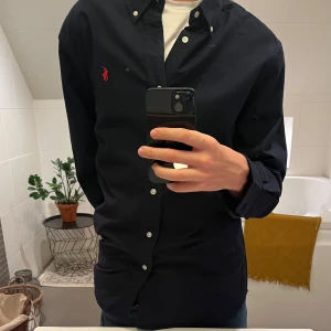 Mörkblå skjorta från Ralph Lauren - Säljer en stilren mörkblå skjorta från Ralph Lauren i nytt skick (aldrig använd) prislapp kvar!🔥 Skjortan har en klassisk design med knappar och en röd broderad logga på bröstet. Perfekt för både vardag och fest! nypris:1699kr Mitt pris:499kr👑Kontakkta för minsta funderingar.