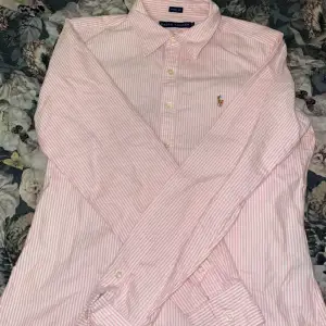 Säljer en snygg rosa och vit randig skjorta från Ralph Lauren i skinny fit. Skjortan har långa ärmar och klassiska knappar framtill. Den är broderad med den ikoniska loggan på bröstet. Perfekt för både vardag och fest!