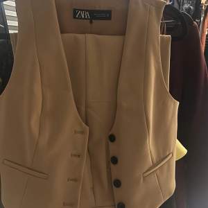 Snygg beige väst från Zara i ett stilrent och klassiskt snitt. Västen har knappar framtill och är perfekt för både vardag och fest. Den är i ett mjukt material som ger en bekväm passform. Passar bra till både byxor och kjol för en chic look.