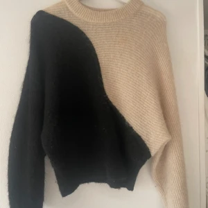 Vit och svart stickad tröja - Säljer den populära och efterfrågade vita  och svarta tröjan från other stories. Den har en unik asymmetrisk design med en lång ärm i varje färg. Perfekt för att hålla sig varm och stilren under hösten och vintern. Passar både till vardags och lite mer uppklädda tillfällen!