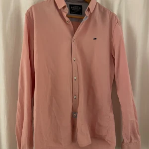 Rosa skjorta från Bondelid - Säljer en snygg rosa skjorta från Bondelid i storlek medium. Skjortan är långärmad och har en klassisk krage med knappar hela vägen ner. Den är tillverkad i ett mjukt bomullsmaterial. Finns knappast tecken på användning utan är i ett bra skick.