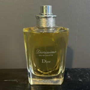 Diorissimo Eau de Toilette från Dior - Säljer en elegant flaska Diorissimo Eau de Toilette från Dior. Flaskan är stilrent designad i glas med en silverfärgad spraytopp och ett vackert mönstrat band runt halsen. Perfekt för den som älskar klassiska och tidlösa dofter. Passar både till vardags och fest. En riktig pärla för parfymälskare! 🌸