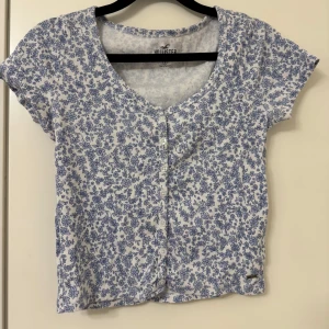 Blommig kortärmad topp från Hollister - Söt blommig topp från Hollister i vitt och blått. Superfin och i mycket bra skick säljer endast då den inte passar längre.