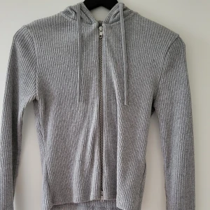 Grå ribbad hoodie från Gina Tricot - Säljer en snygg grå ribbad hoodie från Gina Tricot i storlek S. Den har en dragkedja framtill och en mysig huva. Storlek: S  Skickas inslagen i silkespapper i vattentätt paket.   Skicka pm för fler bilder. 
