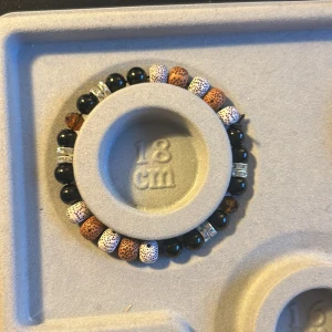 Armband med svarta och bruna pärlor - Snyggt armband med en mix av svarta, bruna och vita pärlor. De bruna pärlorna har ett prickigt mönster och de svarta är glansiga. Mellan pärlorna finns silverfärgade detaljer som ger en extra touch. Perfekt för både vardag och fest!