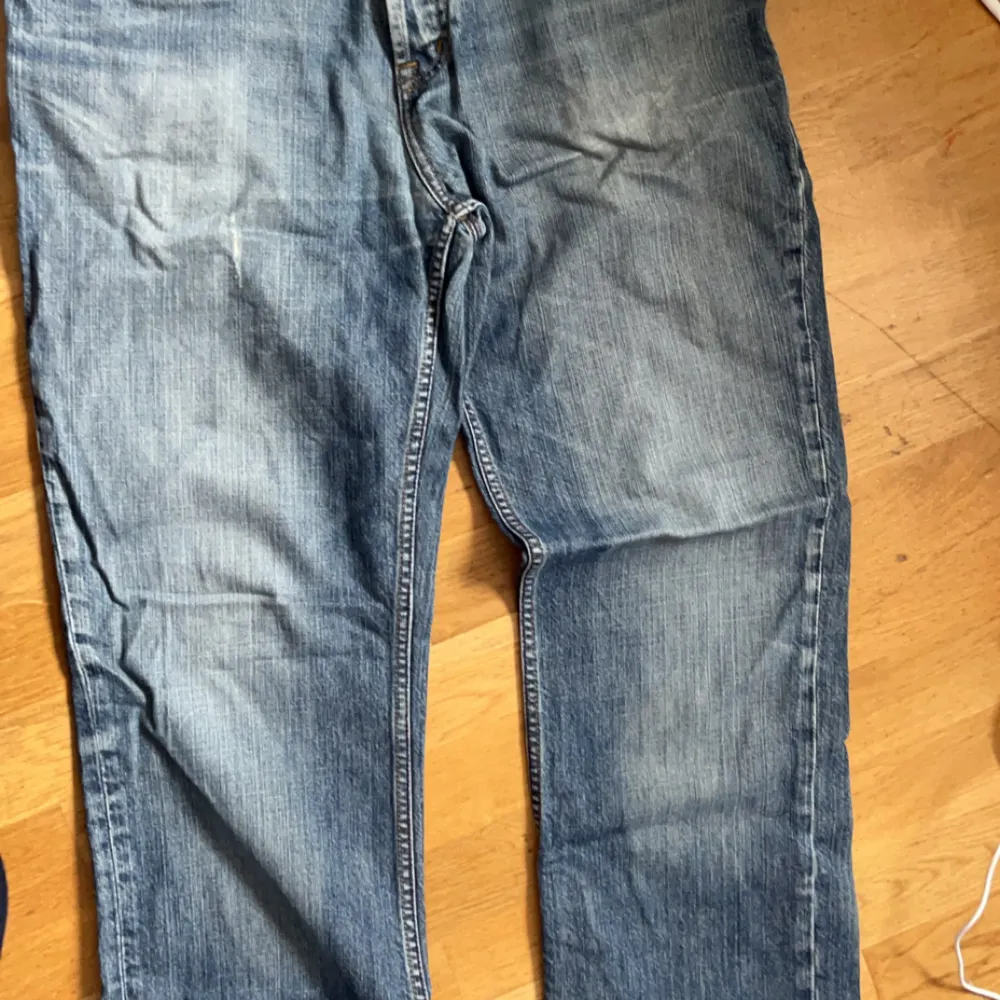 Säljer ett par klassiska blå jeans från Munk. De har en snygg slitning och är i bra skick. Perfekta för vardagsbruk med en normal passform och låg midja. Passar perfekt till både t-shirt och skjorta!. Jeans & Byxor.