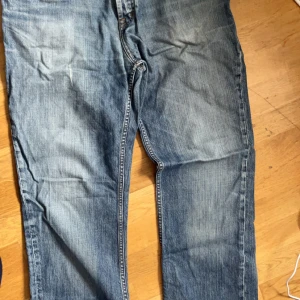 Blå jeans från Munk - Säljer ett par klassiska blå jeans från Munk. De har en snygg slitning och är i bra skick. Perfekta för vardagsbruk med en normal passform och låg midja. Passar perfekt till både t-shirt och skjorta!