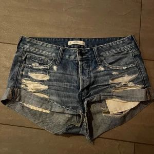 Blå jeansshorts med slitningar - Säljer ett par coola blå jeansshorts med slitningar och råa kanter. Perfekta för en avslappnad sommarlook! De har en klassisk femficksdesign och är lågmidjade för en bekväm passform. Passar perfekt till en sommardag!🫶🏼❤️🩷midjemåttet tvärs över är 44cm🫶🏼
