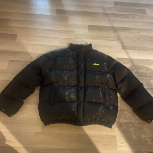(LARGE) Corteiz pufferjacka - Säljer en svart pufferjacka från Corteiz med en cool gul insida. Jackan har broderad text på ryggen och är perfekt för kalla dagar. Jag har använt den 1 gång så den är i väldigt bra skick! Och så har den en oversized passform. Perfekt för vintern! Säljer pga att den inte passade mig.