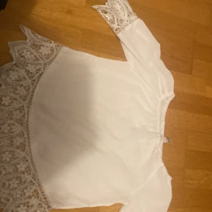 Vit blus med spetsdetaljer - Säljer en superfin vit blus med vackra spetsdetaljer vid ärmslut och nederkant. Blusen har trekvartsärmar och en lös passform, perfekt för vår och sommar. Den är i mycket bra skick och passar både till vardags och festliga tillfällen.