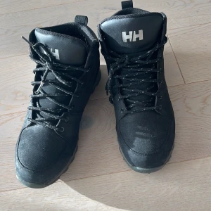 Svarta kängor från Helly Hansen - Säljer ett par svarta kängor från Helly Hansen i mycket bra skick. De har en robust design med snörning och är perfekta för höst och vinter. Skorna är gjorda i syntetmaterial och har en slitstark sula för bra grepp. Perfekta för utomhusaktiviteter i kallare väder!
