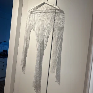 Vit glittrig nätklänning - Säljer en superfin vit nätklänning med glittriga detaljer. Den är långärmad och perfekt för festliga tillfällen. Klänningen är i ett transparent material som ger en cool look över en annan klänning eller outfit. Perfekt för att sticka ut på festen! Storlek M/L (36-40) är stretchig! 