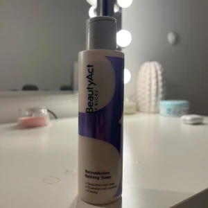 BeautyAct by Kicks RetinolAction Refining Toner - En toner från BeautyAct by Kicks som heter RetinolAction Refining Toner. Den kommer i en stilren flaska med lila och vita detaljer. Tonern är designad för att jämna ut fina linjer, främja cellförnyelse och ge en fastare hud.