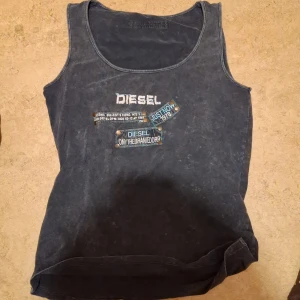 Svart linne från Diesel - Coolt svart linne från Diesel med tryck och nitar på framsidan. Perfekt för en avslappnad stil eller en utekväll. Linnet har en vintage-look med en tvättad finish.