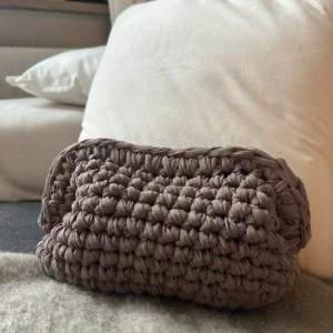 Ljusbrun virkad väska - Säljer en superfin handgjord virkad väska i en mjuk brun nyans. Perfekt för att förvara småsaker eller som en unik accessoar. Den är stickad med tjockt garn vilket ger en mysig och robust känsla. Perfekt för höst och vinter!