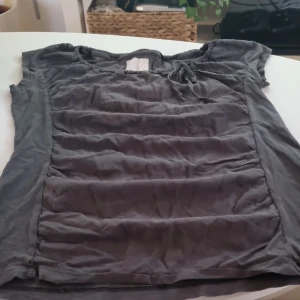 Grå topp med knytband - Säljer en grå topp i bomull med korta ärmar och knytband vid halsen. Perfekt för en avslappnad stil. Toppen är i bra skick och passar till både vardag och fest.