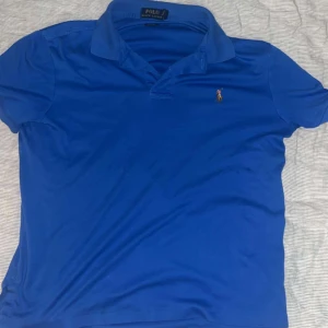 Blå pikétröja från Polo Ralph Lauren - Säljer en klassisk blå pikétröja från Polo Ralph Lauren. Den har korta ärmar och en liten broderad logga på bröstet. Perfekt för en avslappnad men stilren look. Passar både till vardags och lite finare tillfällen.